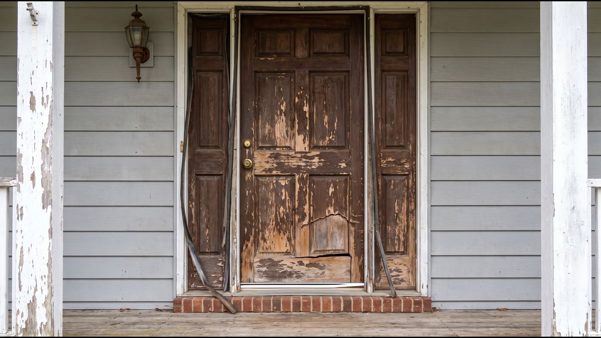 A weathered front door with peeling finish and worn hardware before restoration