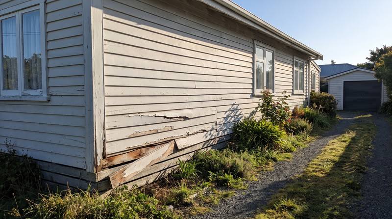 A house wall with cracked and loose lap siding boards before repair