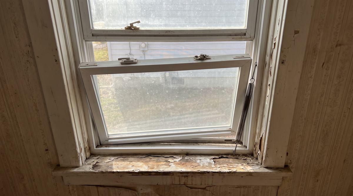 A double hung window with a fallen sash, broken balance and peeling, rotted sill before repair